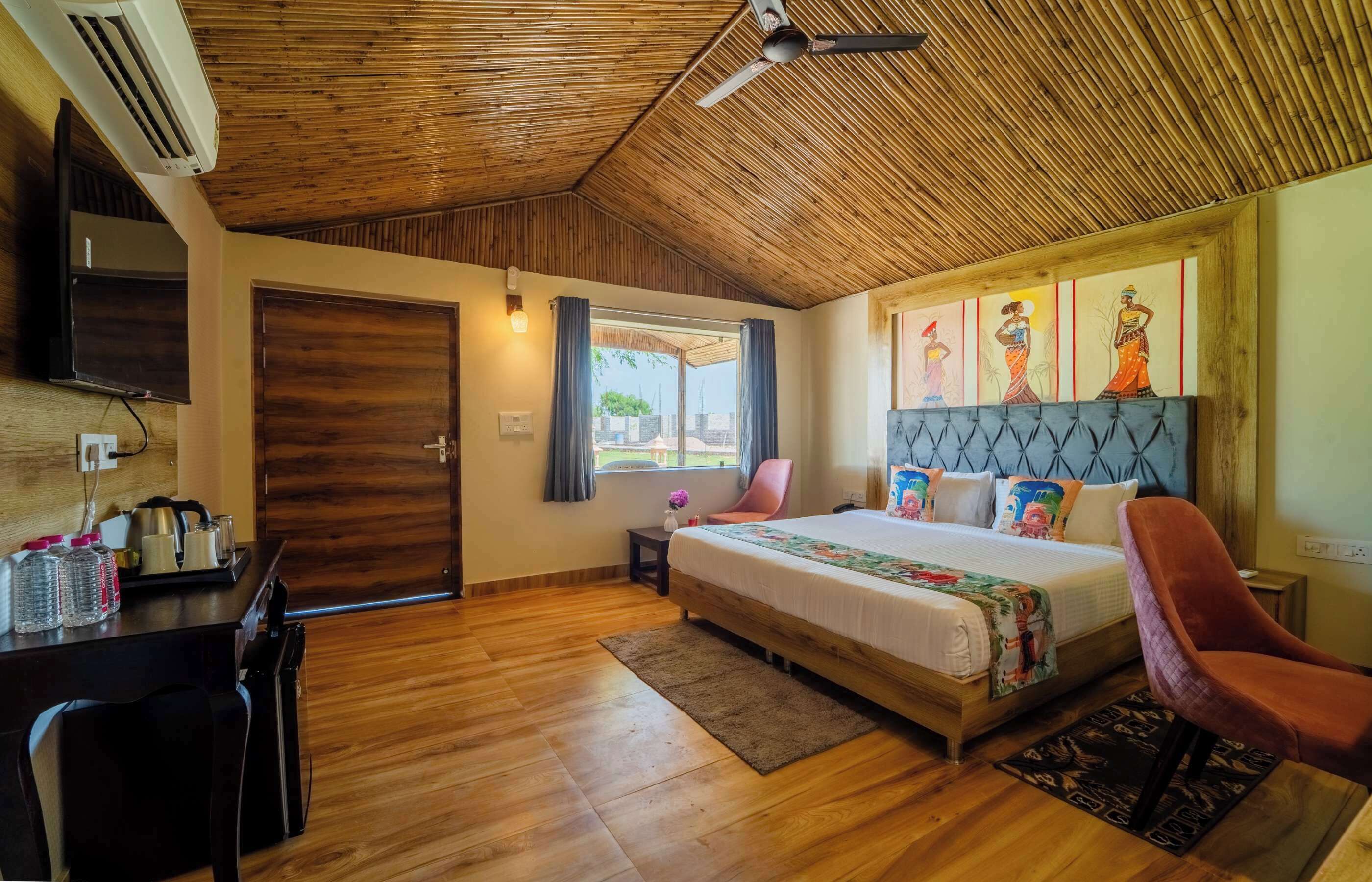 Un dormitorio con techo de madera, una cama con cabecera colorida, un escritorio con silla y un televisor en la pared.