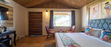 Une chambre avec un plafond en bois, un lit avec une literie aux couleurs vives, un bureau avec une bouilloire et un téléviseur fixé au mur.