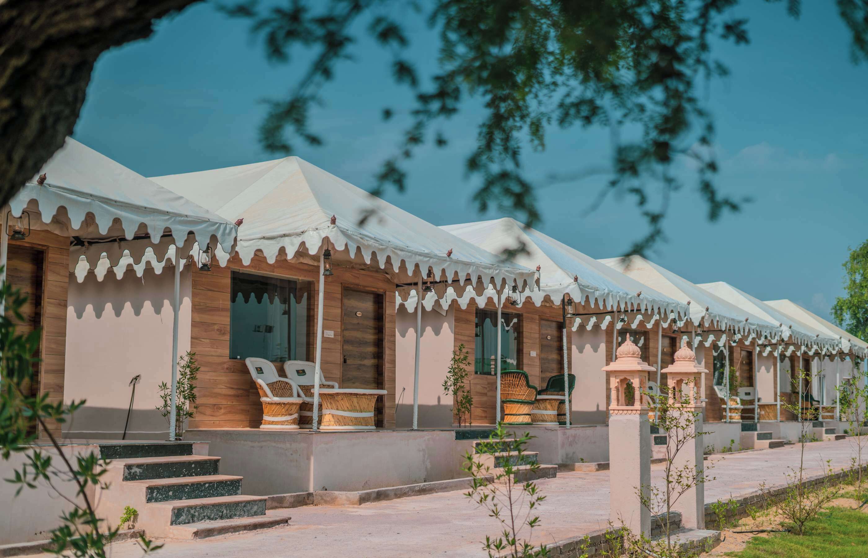 A row of traditional-style guest rooms with white canopies, wooden doors, and wicker furniture.