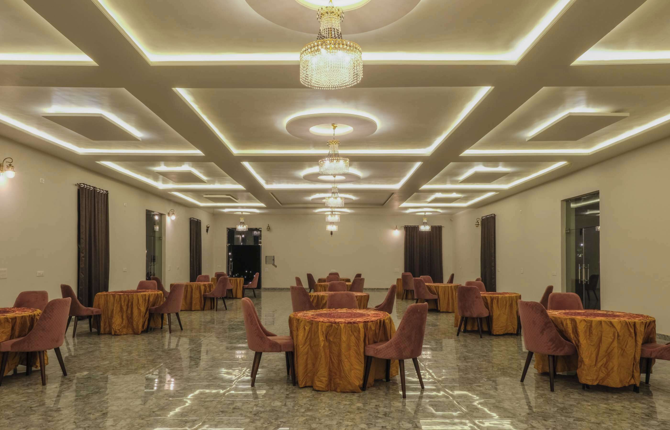 A spacious banquet hall with round tables and chairs, recessed lighting, and a chandelier.
