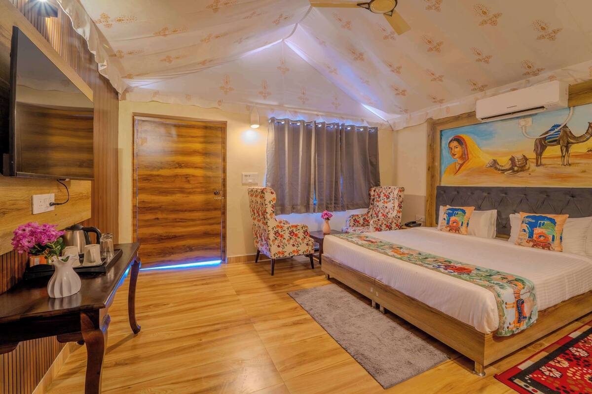 A hotel room with a wooden floor, a bed with floral bedding, a desk with a vase of flowers, and a wall-mounted TV.