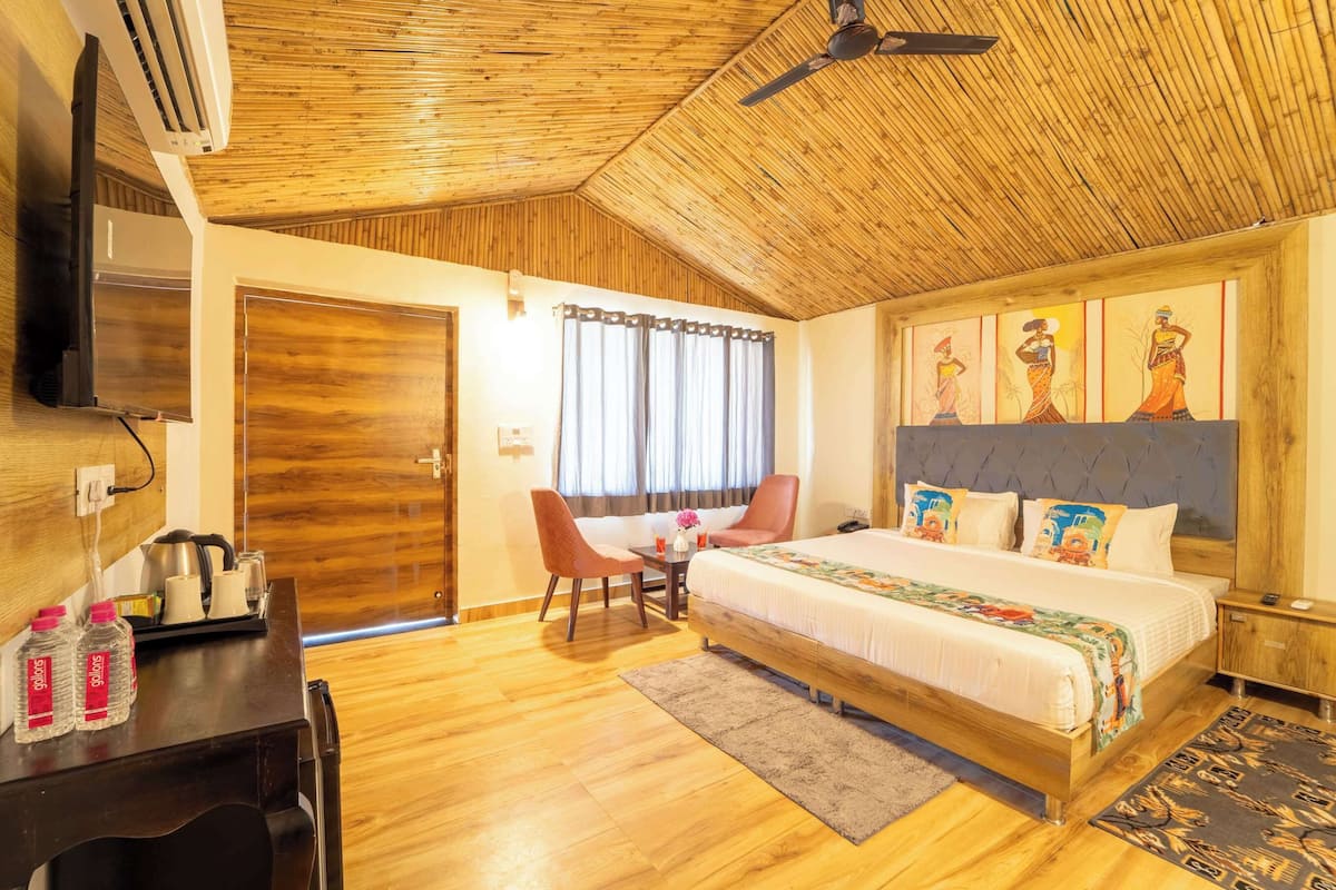 A hotel room with a wooden ceiling, a bed with colorful bedding, a desk with a chair, a television, and a window with curtains.