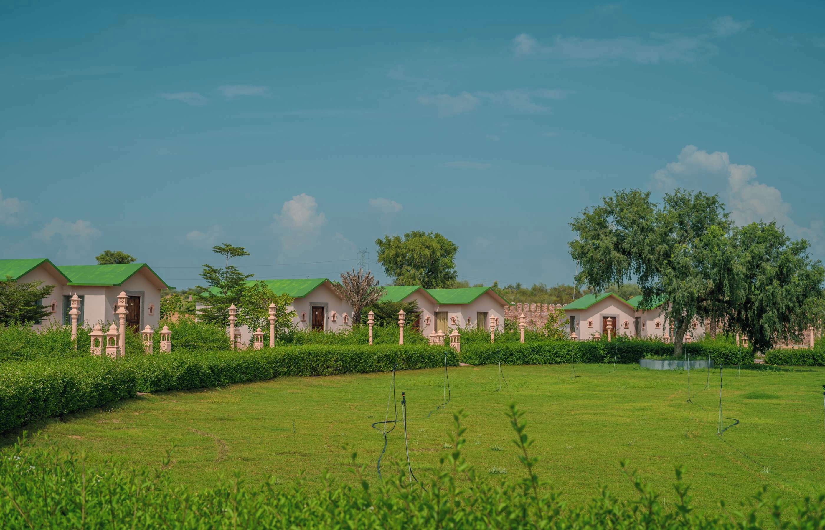 A row of traditional-style cottages with green roofs, surrounded by well-maintained lawns and trees.