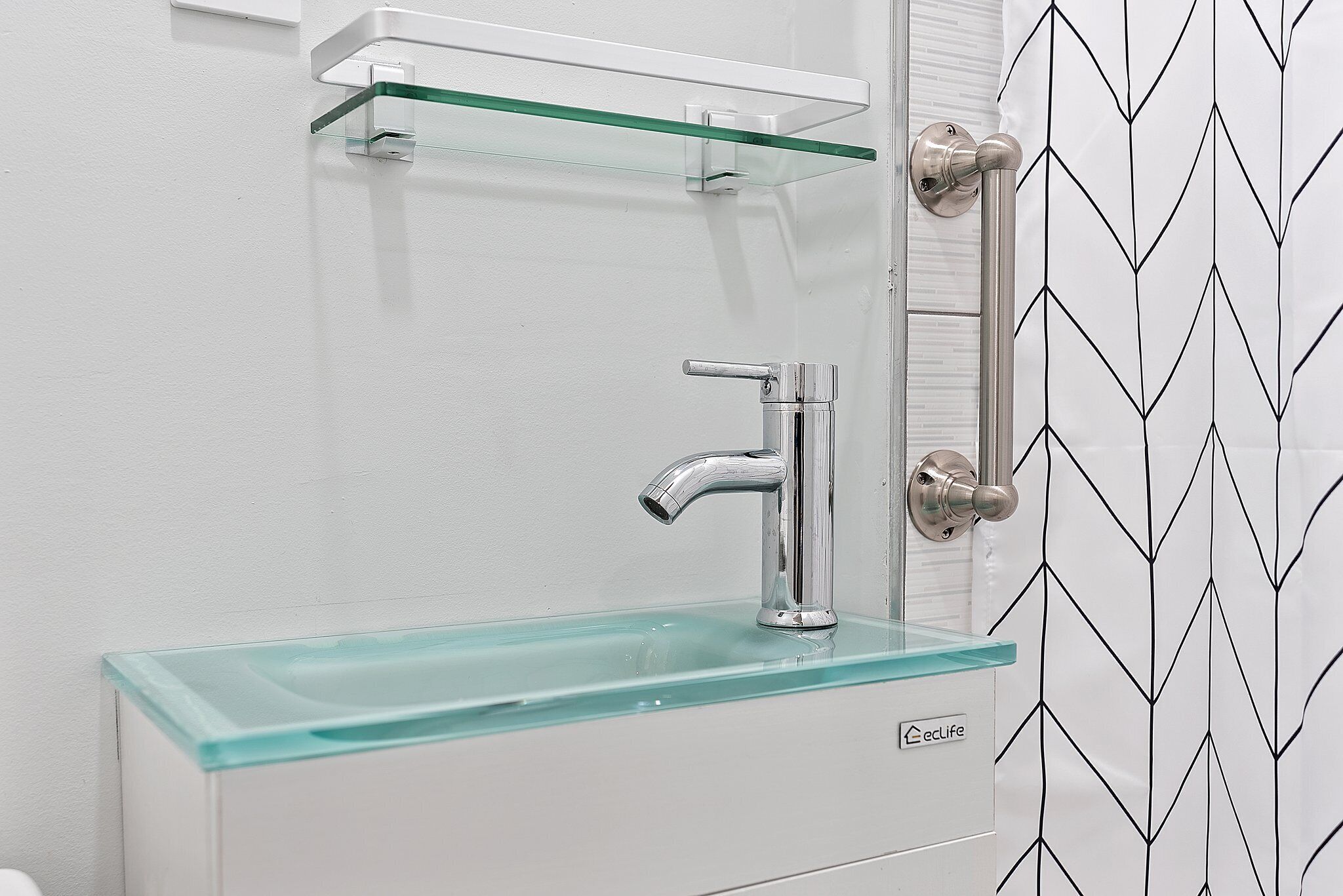 A bathroom with a glass shelf above a sink, a modern faucet, and a door with a geometric pattern.