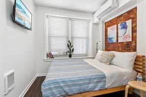 Ein Schlafzimmer mit einem Bett, einem Fenster mit Jalousien, einem Blumentopf und Kunstwerken an der Wand.