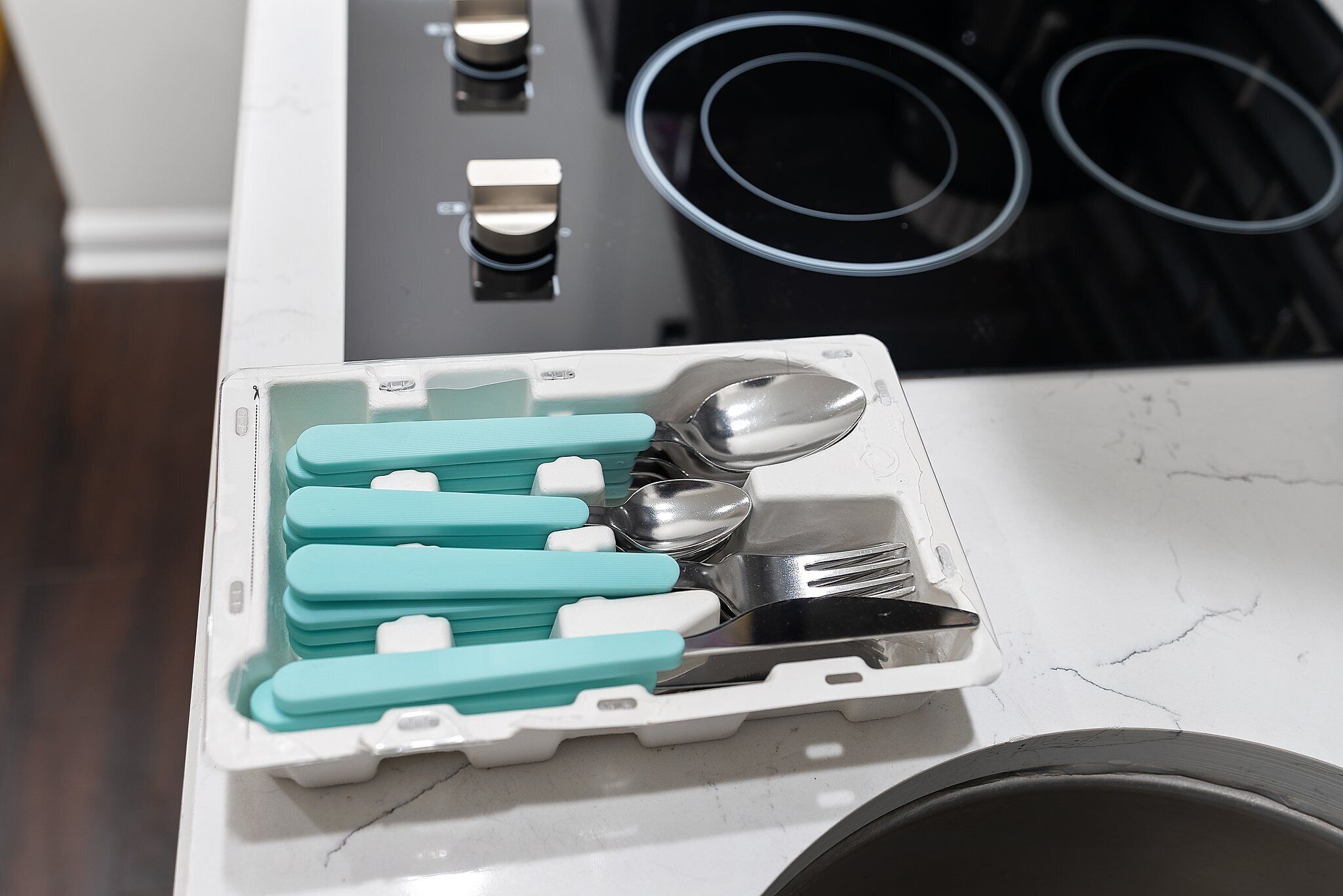 Uma bancada de cozinha com superfície de mármore branco, fogão preto e uma bandeja branca com utensílios.