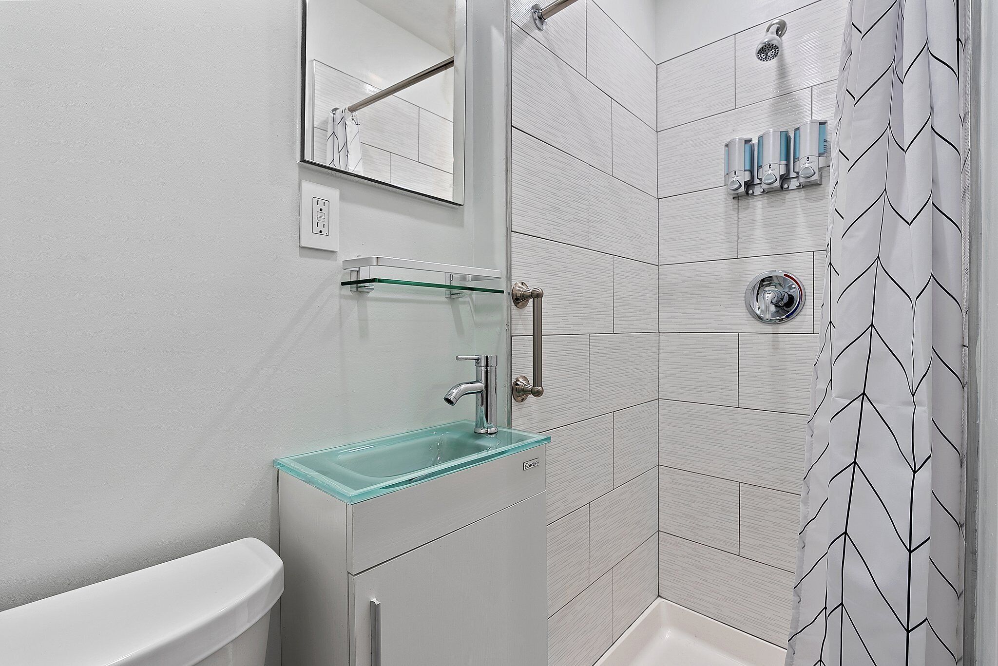 A modern bathroom with a glass sink, a toilet, a shower, and a mirror.