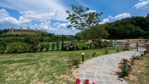 A stone pathway leading to a pool area, surrounded by lush greenery and a castle in the background. - Cosy apartment for 2 guests with A/C, WIFI, pool, TV and pets allowed, close to Siena (Monteriggioni)