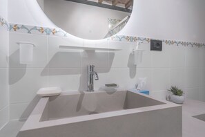 A modern bathroom with a large sink, a mirror, and a potted plant.