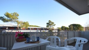An outdoor patio area with a table set for two, white plastic chairs, a wicker basket with flowers, and a white fence in the background.