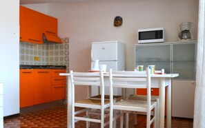 Une cuisine avec des meubles de couleur blanche et orange, un four à micro-ondes, une machine à café et une table à manger avec des chaises.