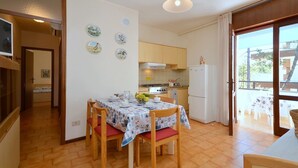 A dining area with a table set for four, a kitchen in the background, and a balcony with outdoor seating.
