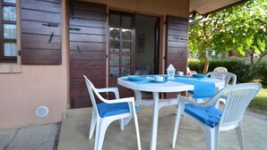 A patio with a round table and four white chairs with blue cushions, a brown door, and a window with blinds. - Stylish villa with communal garden (Bibione)