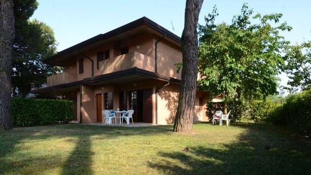 A two-story house with a balcony, a lawn, and trees. - Stylish villa with communal garden (Bibione)