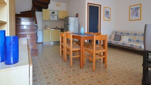 A living room with a dining table and chairs, a sofa, a television, and a kitchen area with a microwave and refrigerator. - Stylish villa with communal garden (Bibione)