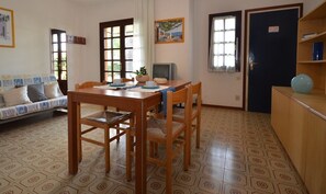 A dining area with a wooden table and chairs, a sofa with patterned cushions, and a television.
