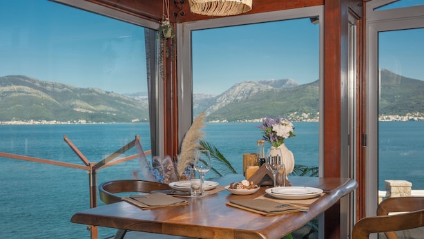Une table à manger avec des chaises, un vase rempli de fleurs et une vue sur la mer et les montagnes.