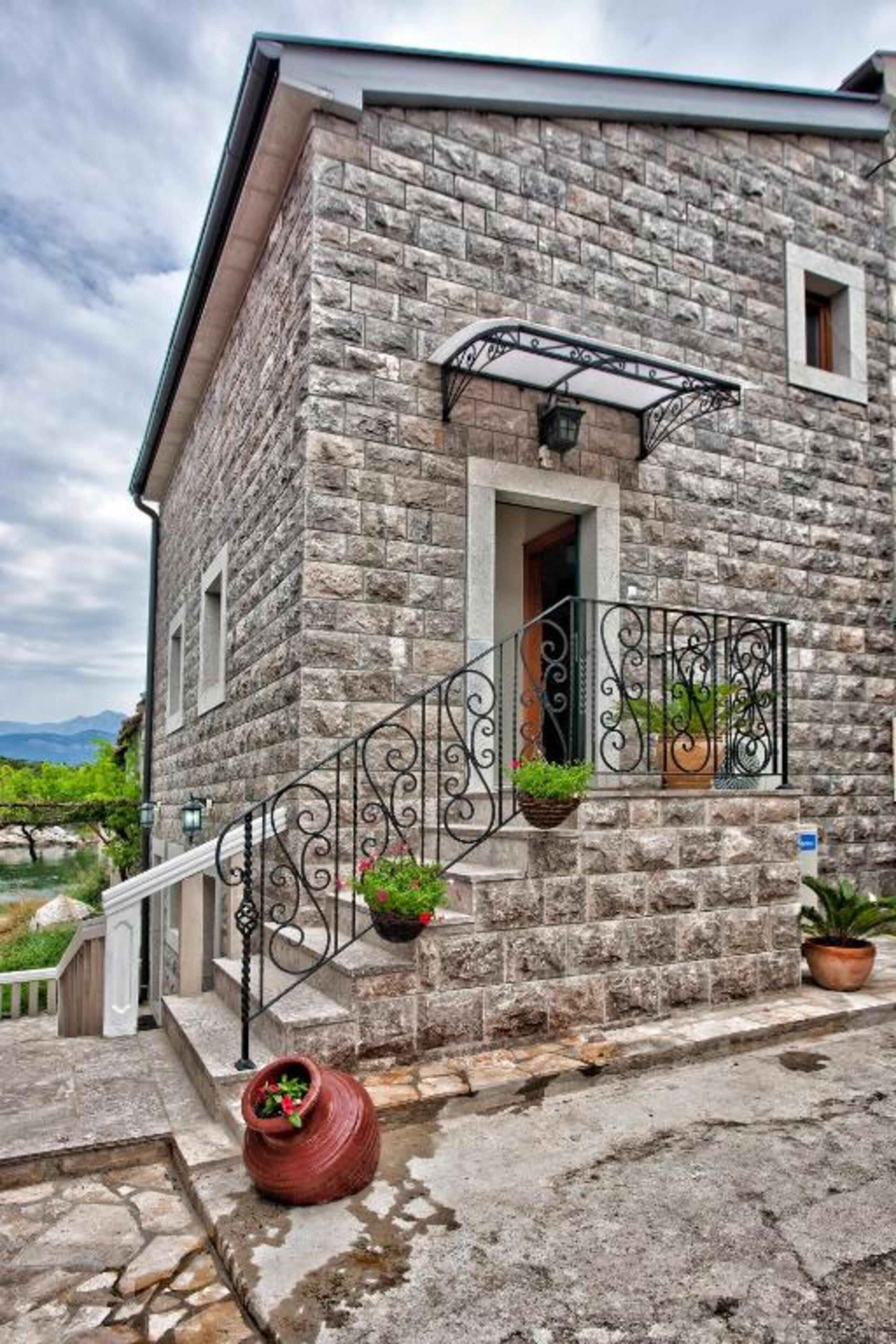 Edificio de piedra con una escalera de metal, plantas en macetas y vistas a las montañas.