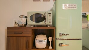 Μια κουζίνα με έναν φούρνο μικροκυμάτων τοποθετημένο πάνω σε ένα ξύλινο ντουλάπι, ένα ψυγείο και μια συσκευή για το μαγείρεμα ρυζιού.