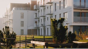 Um edifício residencial moderno de vários andares, com varandas, telhado plano e gramado bem cuidado.