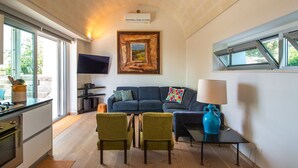 Una sala moderna con un sofá azul oscuro, dos sillones verdes, una mesa de centro, un televisor y un cuadro en la pared.