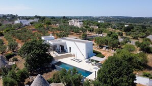 Una villa moderna con piscina, rodeada de olivos y un paisaje montañoso.