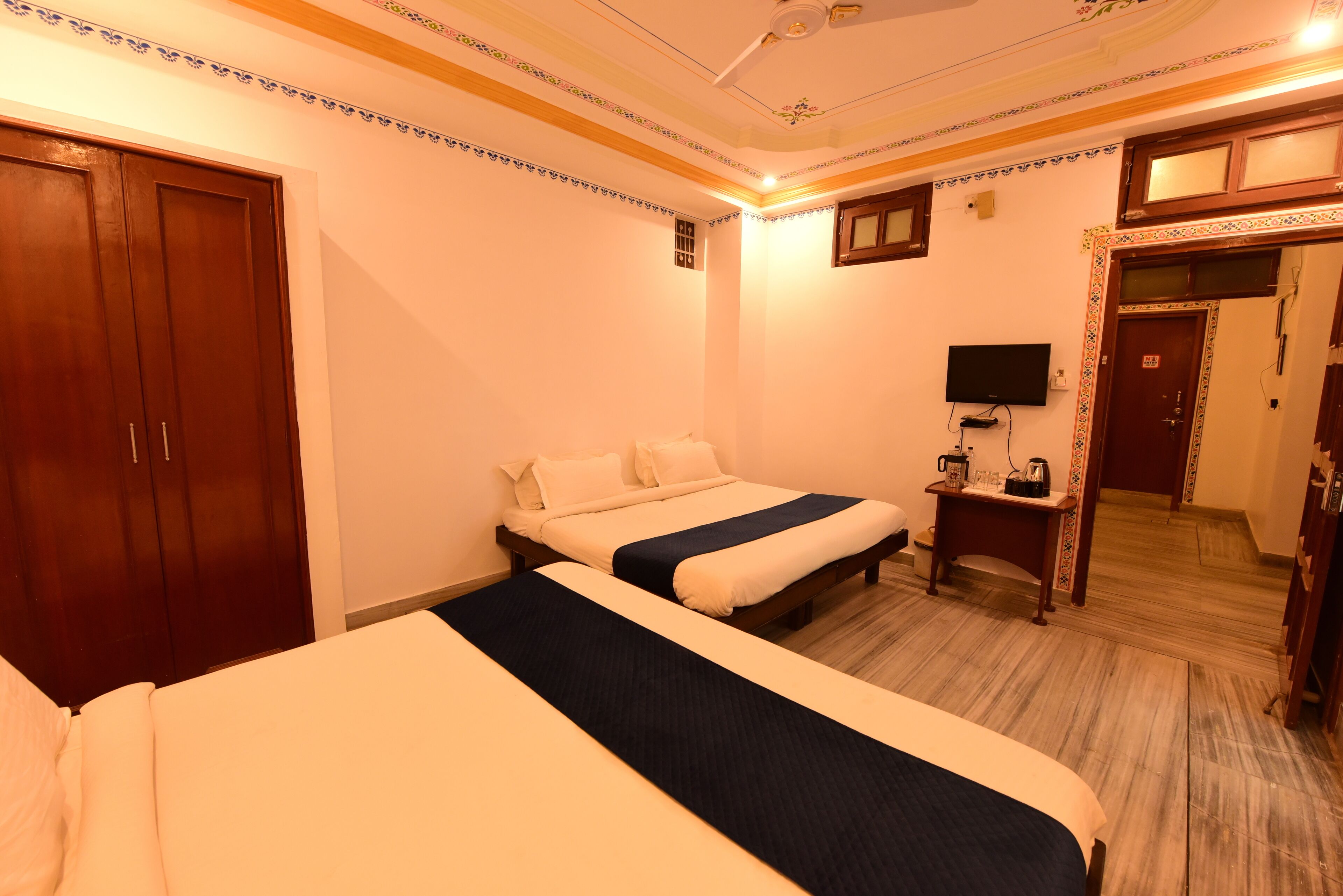 A hotel room with two beds, a television, a desk with a coffee maker, and a wardrobe.