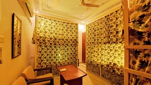 Een kamer met bloemenbehang, een plafondventilator, een klein houten tafeltje en een bank.