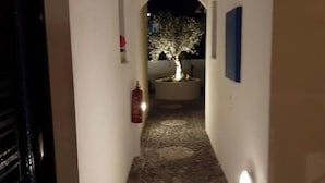 A narrow hallway with a stone floor, an arched doorway at the end, and a lit tree in the center. - Black Beach Village (Santorini)