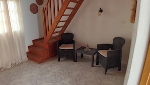 A small, cozy room with a wooden staircase, two chairs, a small table, and a wall-mounted light fixture. - Black Beach Village (Santorini)