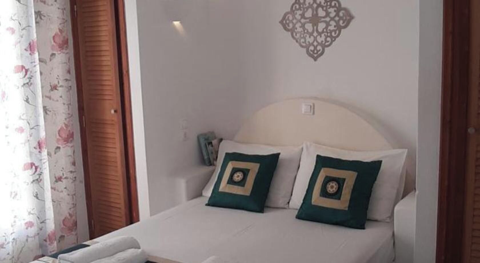 Un letto con due cuscini, una lampada fissata al muro e un elemento decorativo a parete.