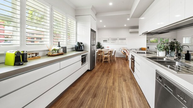 A modern kitchen with white cabinetry, a wooden floor, and a dining area with a table and chairs.