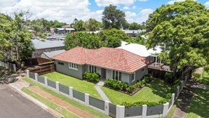 A two-story house with a red-tiled roof, surrounded by a white fence and lush greenery.