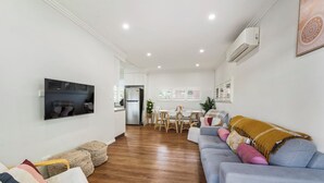 A modern living room with a grey sofa, wooden flooring, a flat-screen TV, and a dining area with a table and chairs.
