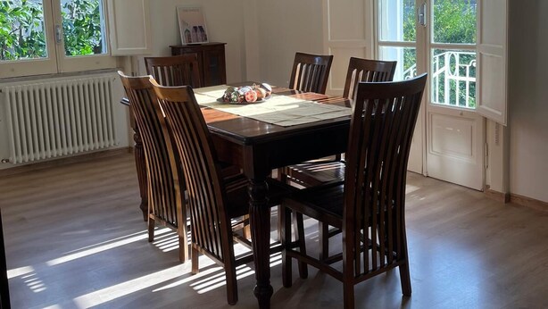 A dining room with a wooden table and chairs, large windows, and a hanging light fixture. - Casa Degli Aranci Charming apartment in the prestigious neighborhood of Vomero (Napoli)