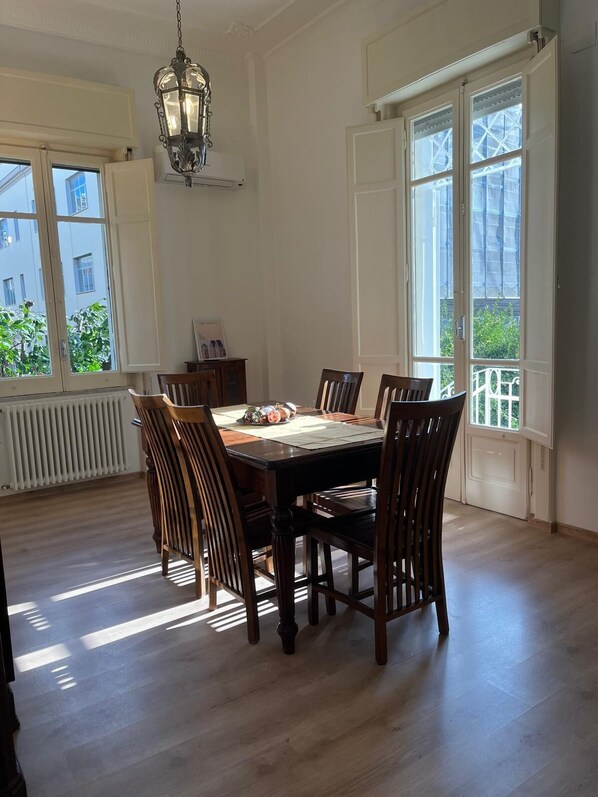A dining room with a wooden table and chairs, large windows, and a hanging light fixture. - Casa Degli Aranci Charming apartment in the prestigious neighborhood of Vomero (Napoli)