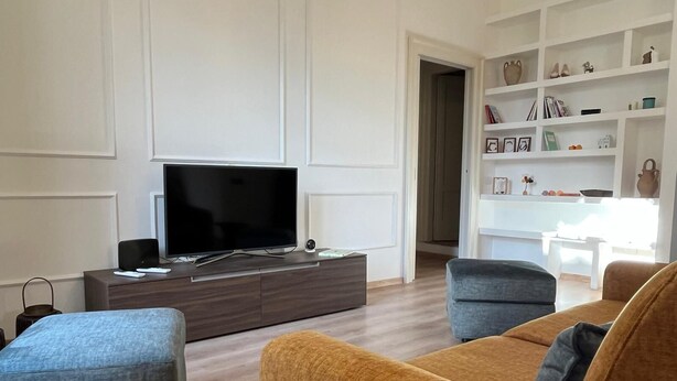 A modern living room with a flat-screen TV on a wooden console, two sofas, and a white shelving unit with decorative items. - Casa Degli Aranci Charming apartment in the prestigious neighborhood of Vomero (Napoli)