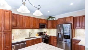 A kitchen with wooden cabinets, a stainless steel refrigerator, a microwave, and a sink. - Spacious 4-bedroom house with hot tub and spa-like backyard. Home away from home (Oceanside)