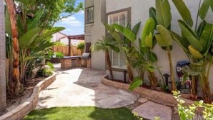A patio with stone flooring, surrounded by lush green plants and a wooden fence. - Spacious 4-bedroom house with hot tub and spa-like backyard. Home away from home (Oceanside)
