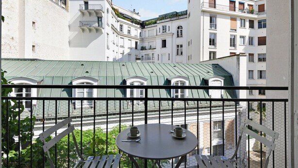 Ein Balkon mit Tisch und Stühlen, der auf einen Innenhof mit Gebäuden blickt.