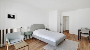 Ein modernes Schlafzimmer mit Bett, Sessel, kleinem Tisch, Nachttisch und Heizkörper.