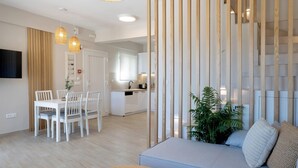 A modern living room with a sofa, dining table, chairs, and a kitchen in the background.