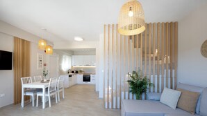 A modern living room with a dining area, a kitchen in the background, and a large window.