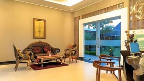 A spacious living room with a large window, a sofa, two armchairs, a coffee table, and a desk with a computer. - WAKAYAPA Syariah Residence (Kelapa Dua)