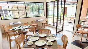 A dining area with multiple tables and chairs, large windows, and a view of the outside. - WAKAYAPA Syariah Residence (Kelapa Dua)