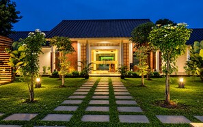A modern building with a tiled roof, a central entrance, and a well-maintained garden with a stone pathway leading to the entrance. - WAKAYAPA Syariah Residence (Kelapa Dua)