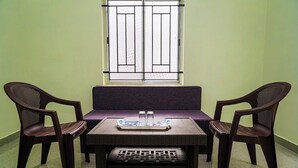 A room with a low table, two chairs, a window with bars, and a small table with two glasses and a tray. - AK Vellore Stays  (Vellore)