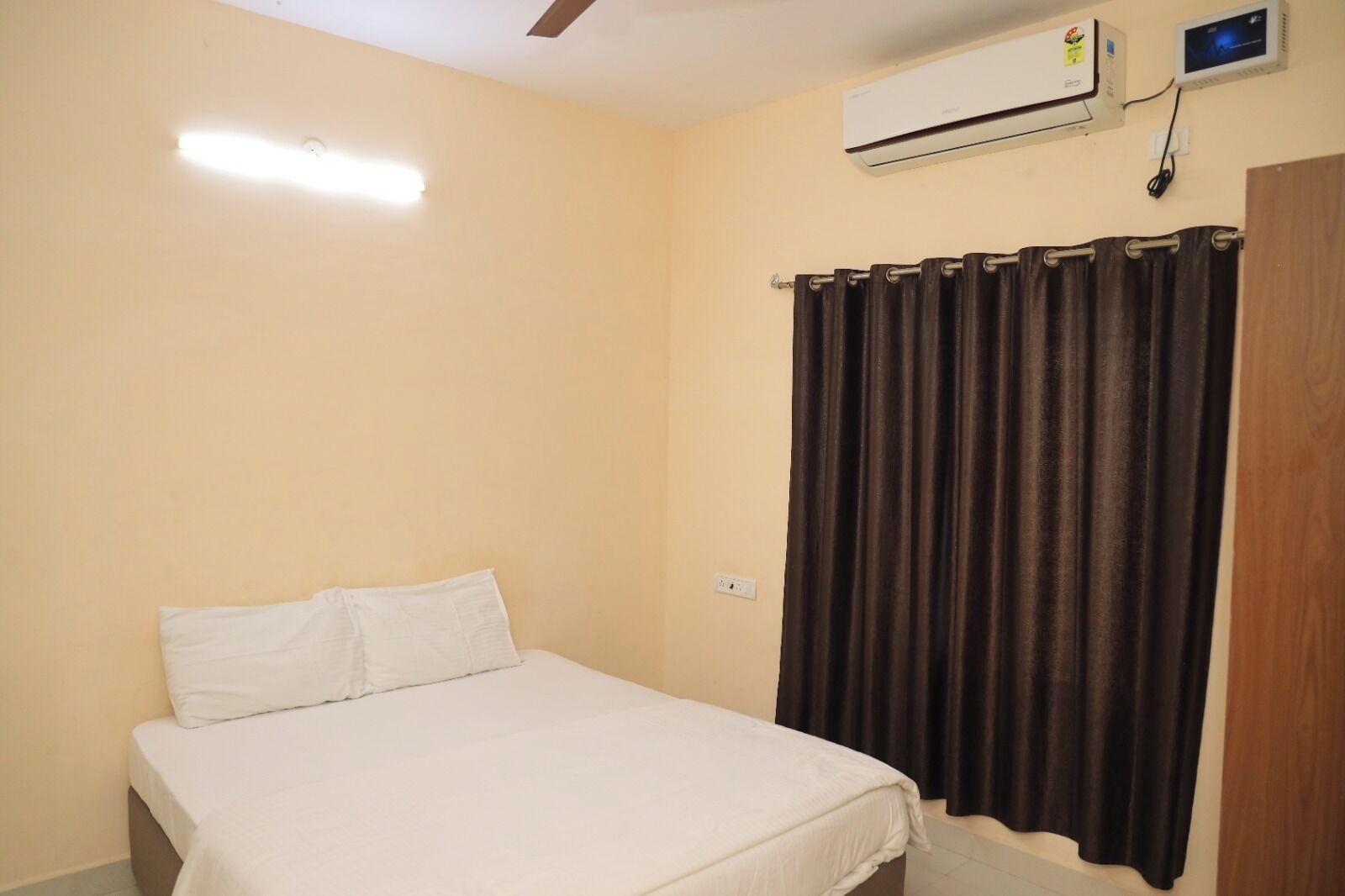 A bedroom with a bed, a ceiling fan, an air conditioning unit, and a curtain.