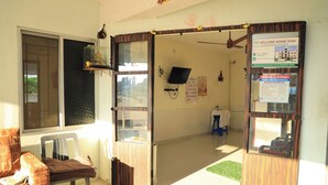 A room with a bed, a chair, a small table, a TV, and a window. - AK Vellore Stays  (Vellore)