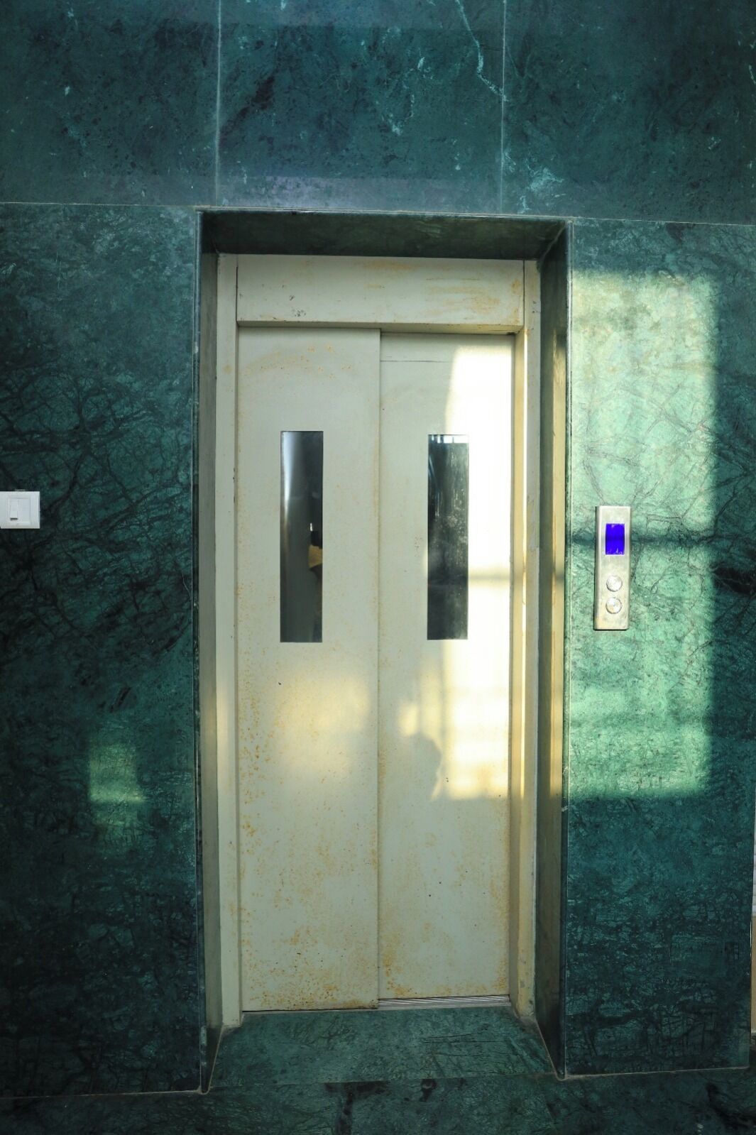 A door with a metal handle and a rectangular panel, set in a wall with a textured surface.
